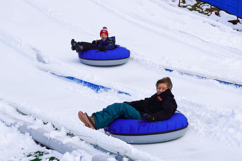 two people riding in tubes down a snowy hill at rowdy bear's smoky mountain snowpark